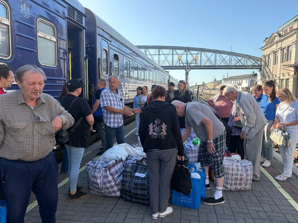Пасажири з багажем біля синього потяга на вокзалі