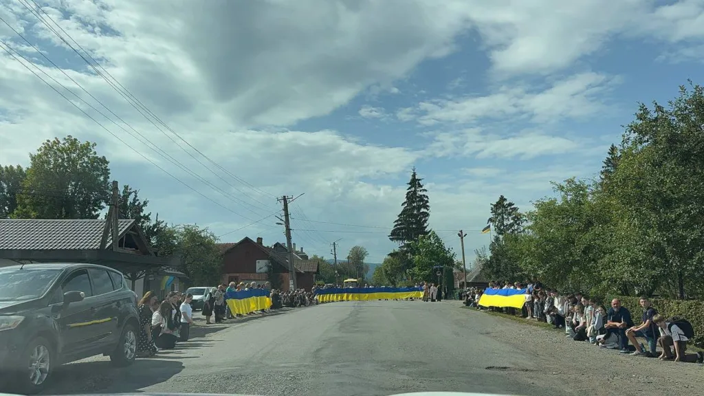 Люди з українськими прапорами вздовж сільської дороги
