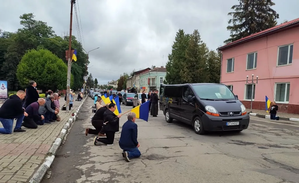 Люди навколішки зустрічають кортеж із українськими прапорами