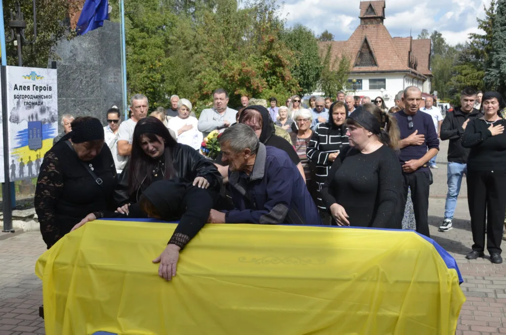 Люди прощаються з військовим біля труни під прапором України