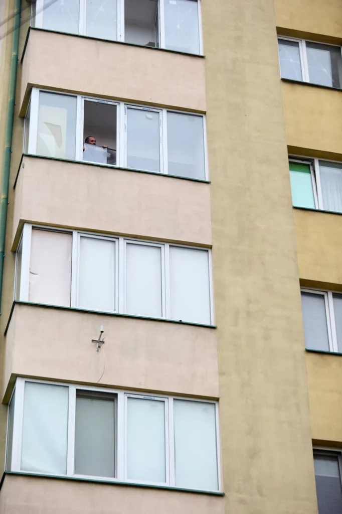 Чоловік визирає з вікна багатоповерхового будинку