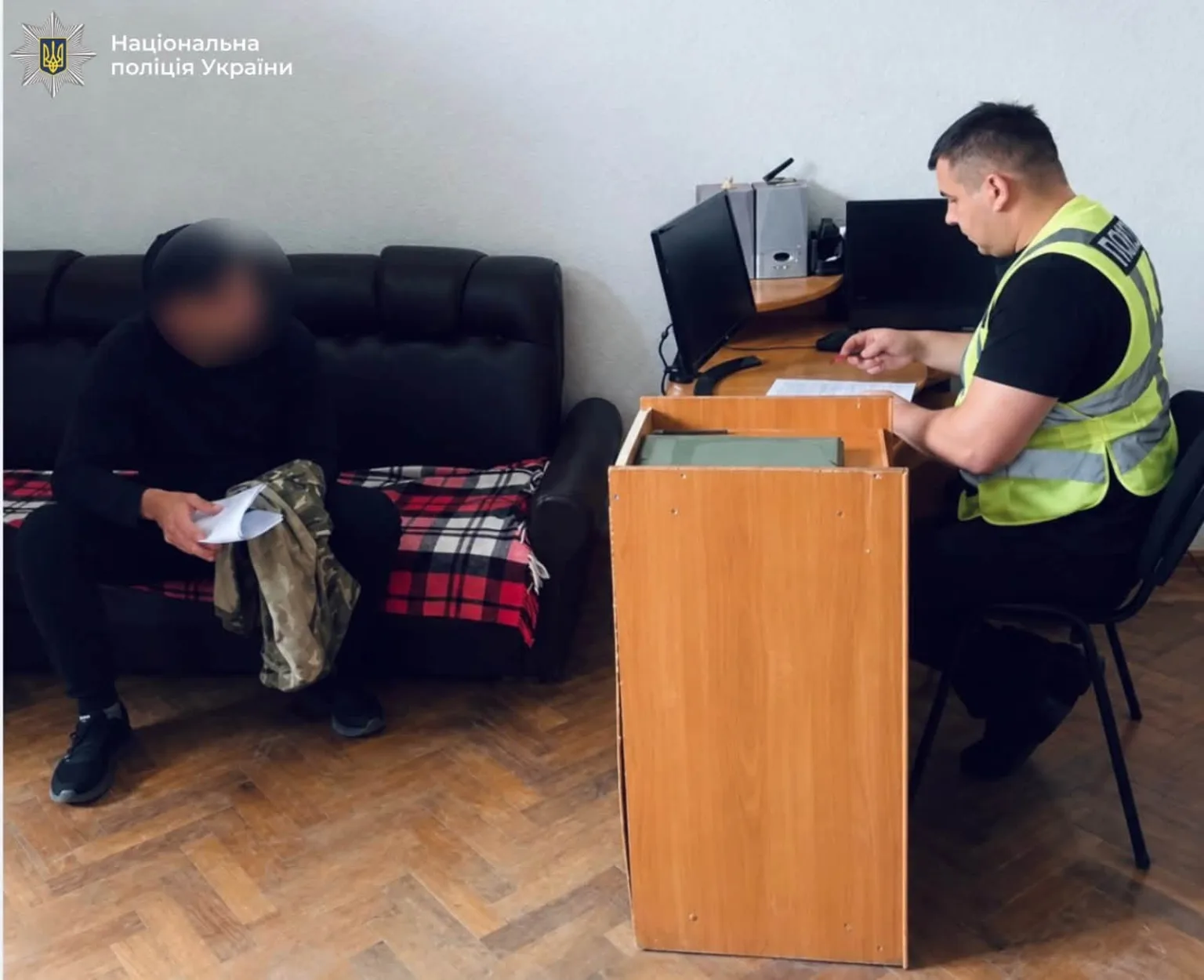 Поліцейський оформлює документи поруч із чоловіком із заблюреним обличчям