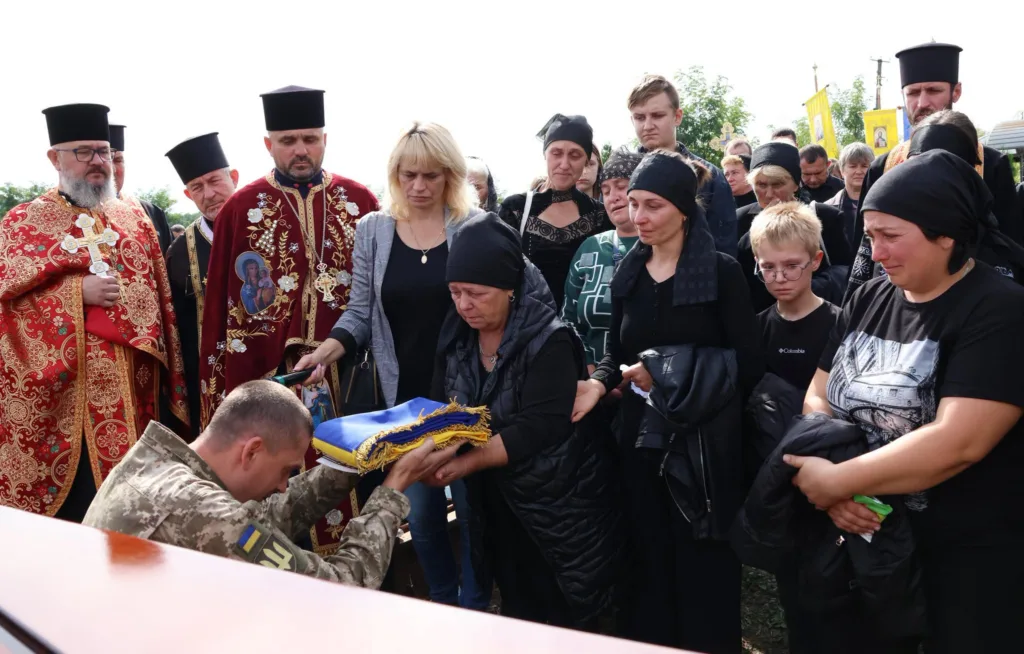 Військовий передає український прапор родині на похороні.