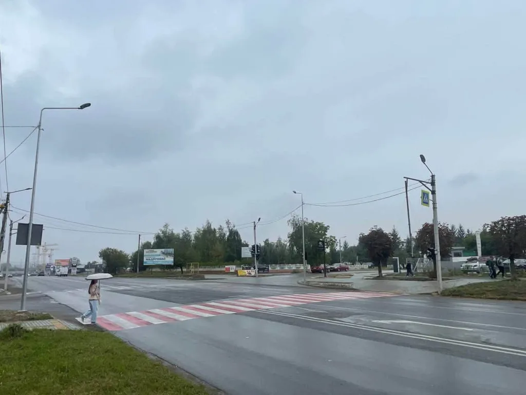 Пішохід з парасолькою біля мокрого переходу в дощ
