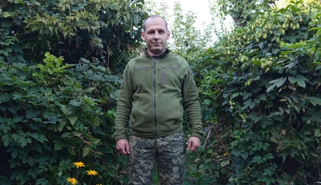 Чоловік у зеленій куртці серед густих заростей хмелю