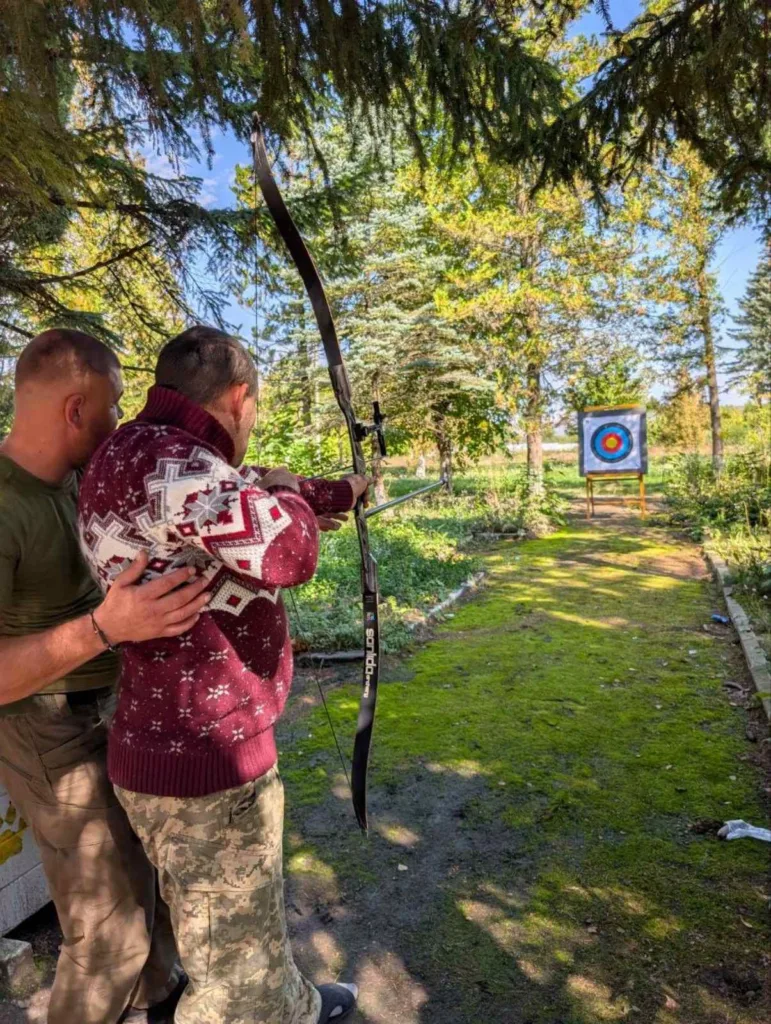 Чоловік навчає іншого стрільбі з лука