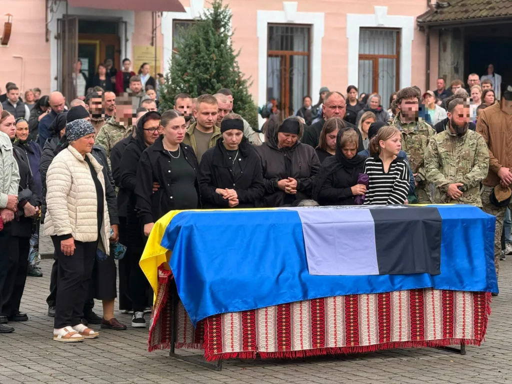 Люди прощаються з військовим біля труни з прапорами