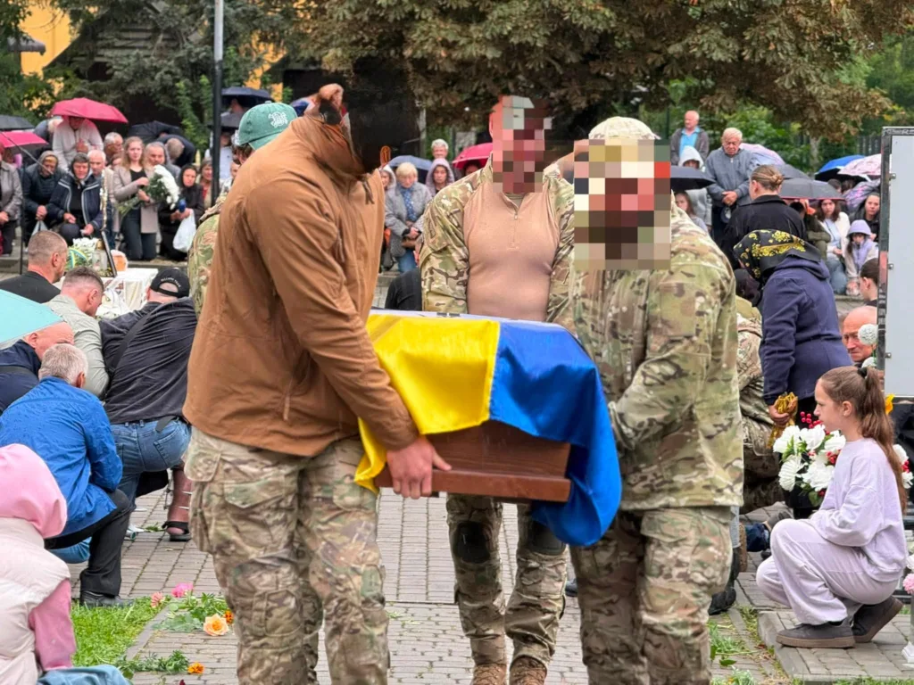 Військові несуть труну, вкриту українським прапором