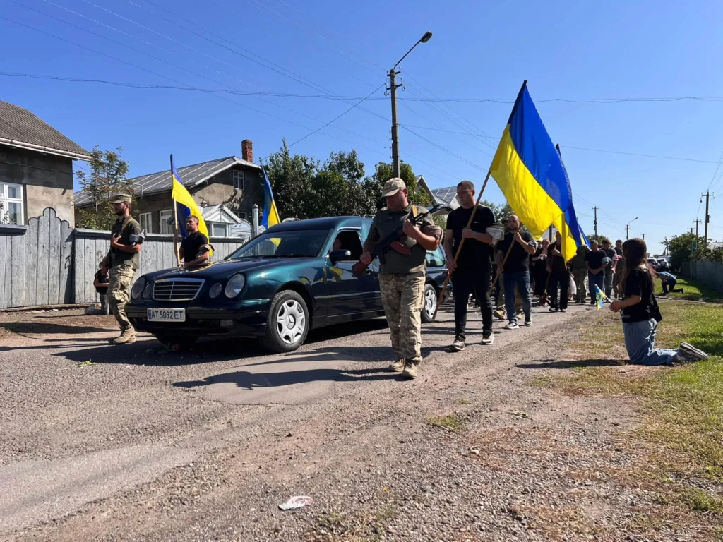 Люди з українськими прапорами супроводжують автомобіль вулицею