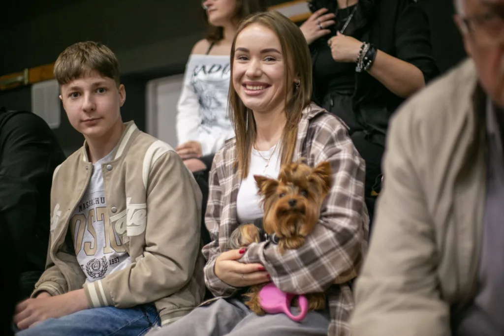 Усміхнена дівчина тримає йоркширського тер’єра серед людей