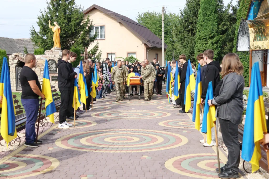 Військові несуть труну між людьми з прапорами України