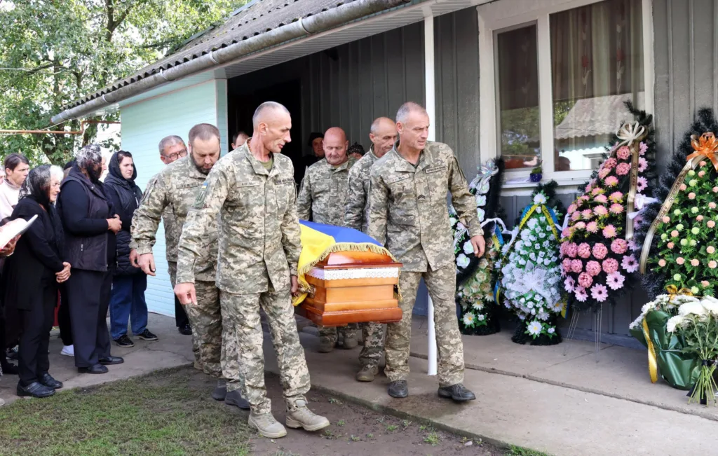 Військові несуть труну, вкриту українським прапором