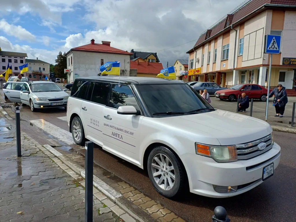 Ритуальні автомобілі з українськими прапорами на міській вулиці