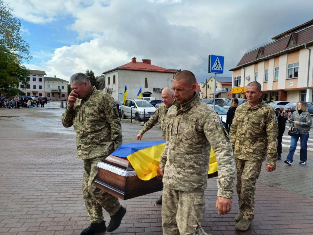Військові несуть труну, вкриту українським прапором
