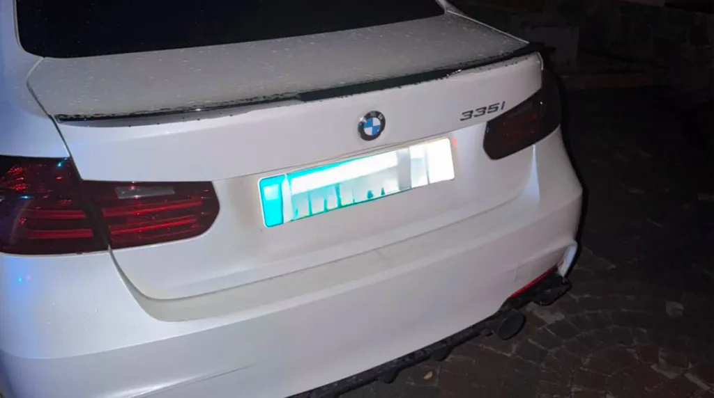 Задня частина білого BMW 335i з підсвіченим номером