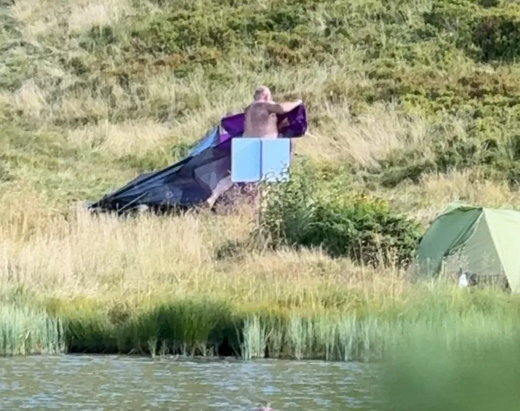 Чоловік встановлює намет на трав’янистому березі водойми