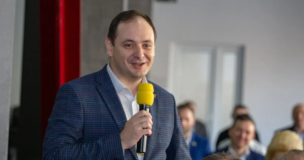 Чоловік у піджаку виступає з жовтим мікрофоном