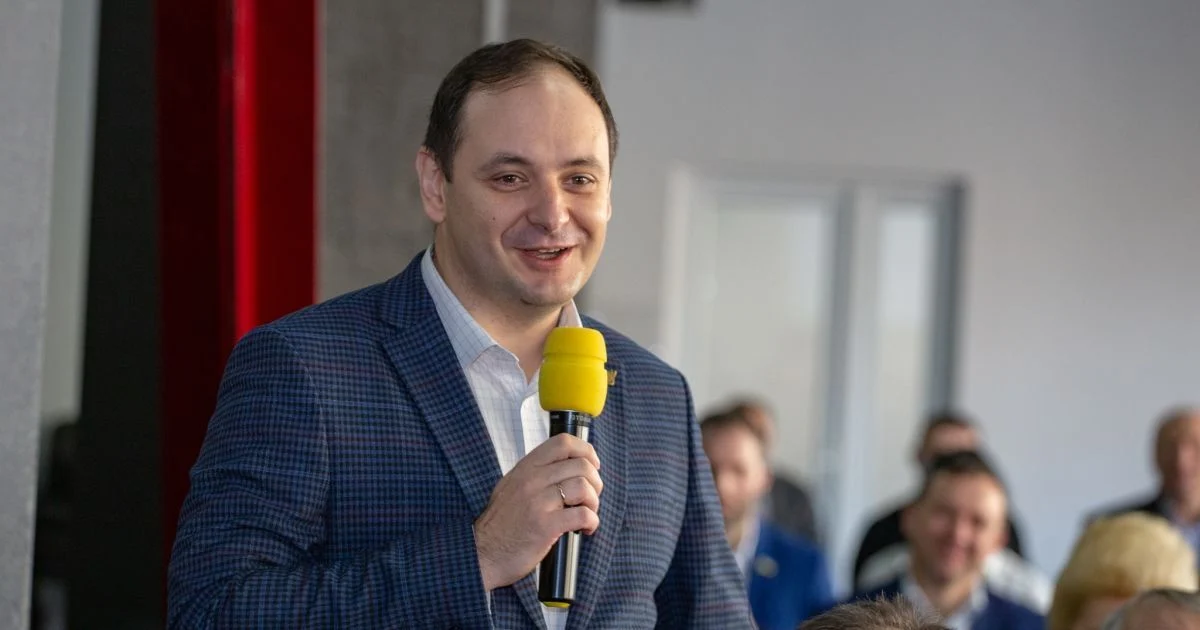 Чоловік у піджаку виступає з жовтим мікрофоном