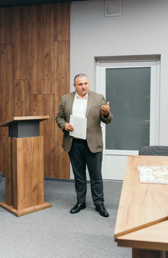 Чоловік виступає з паперами біля дерев’яної трибуни