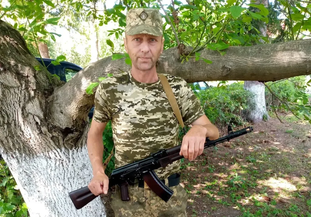 Військовий у камуфляжі тримає автомат біля дерева