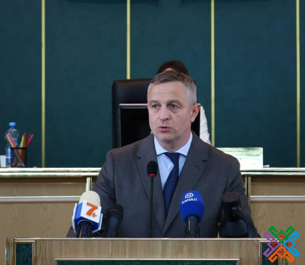 Чоловік у костюмі виступає за трибуною перед мікрофонами