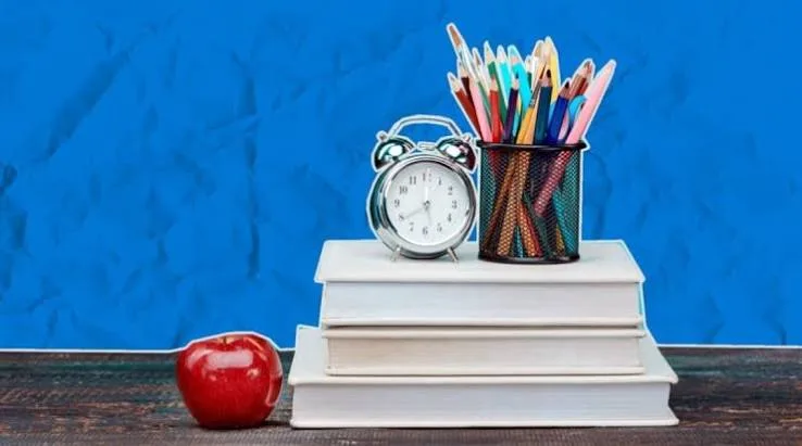 Книги, будильник, олівці та яблуко на синьому тлі