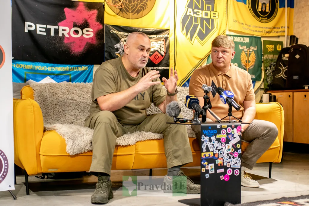 Двоє чоловіків дають інтерв’ю перед військовими прапорами