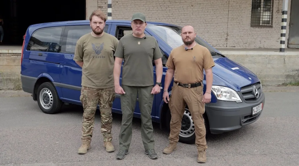 Троє чоловіків стоять перед синім мікроавтобусом Mercedes