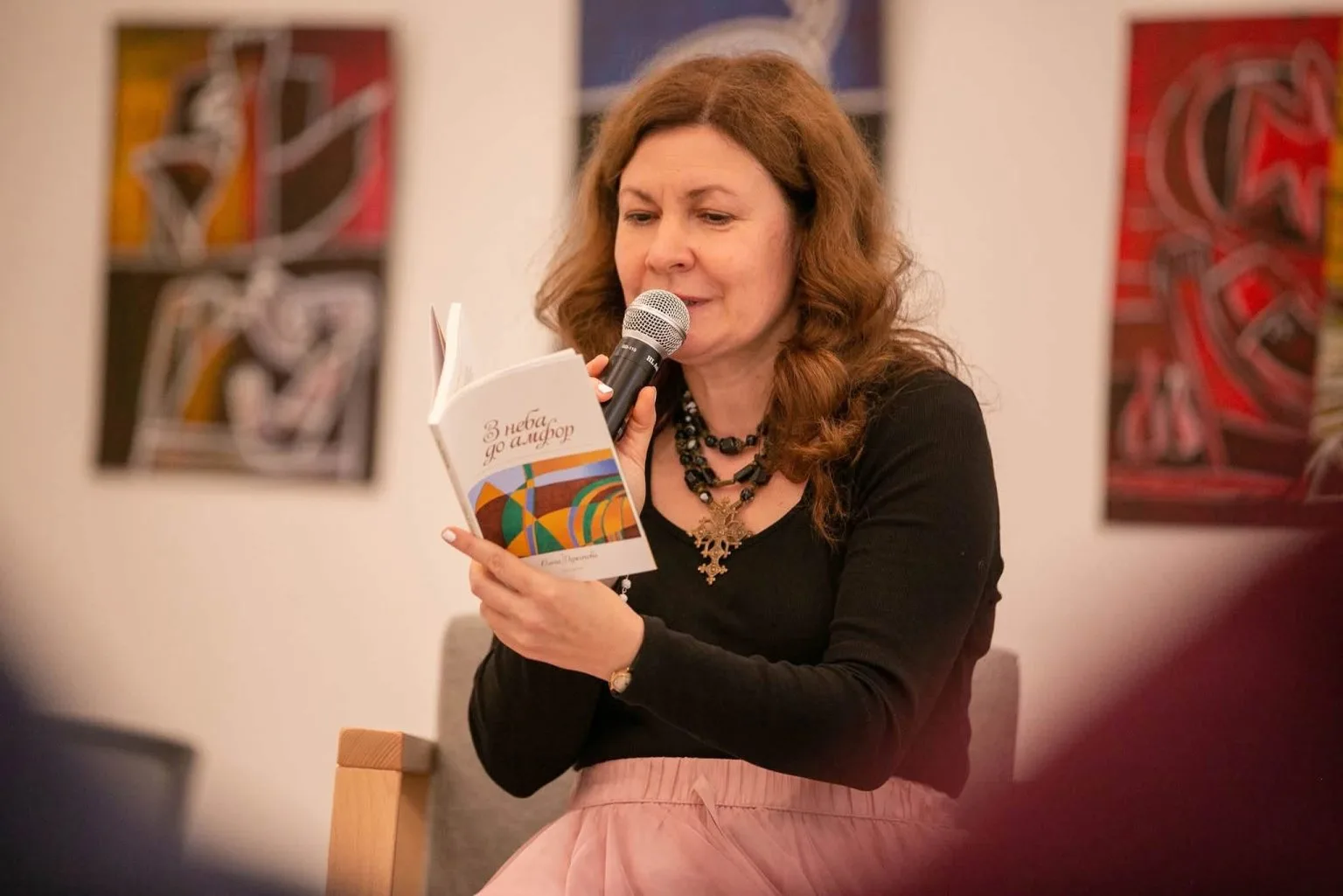 Жінка читає книгу в мікрофон на мистецькому заході