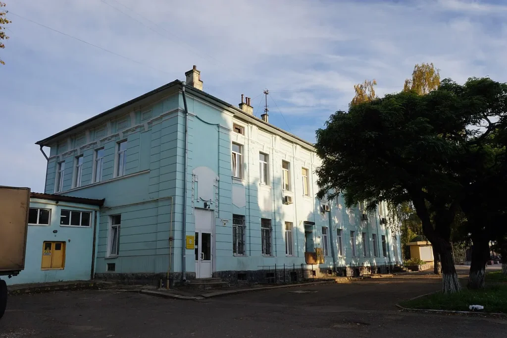 Світло-блакитна двоповерхова будівля біля великих дерев