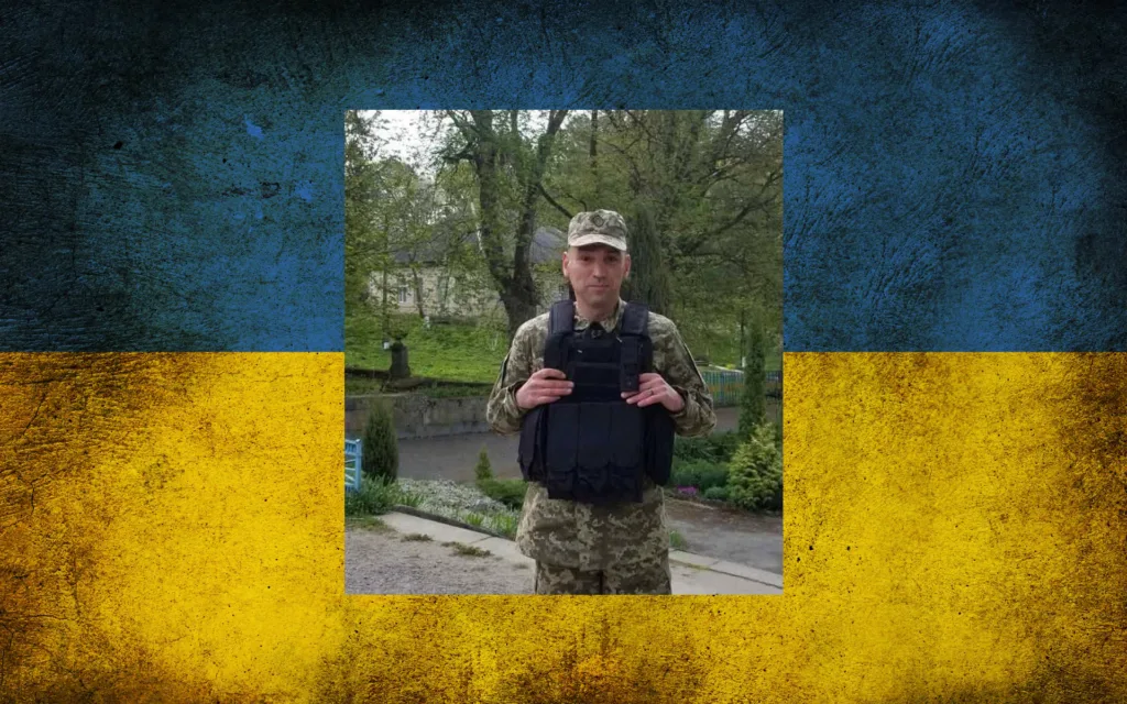 Військовий у бронежилеті на тлі українського прапора