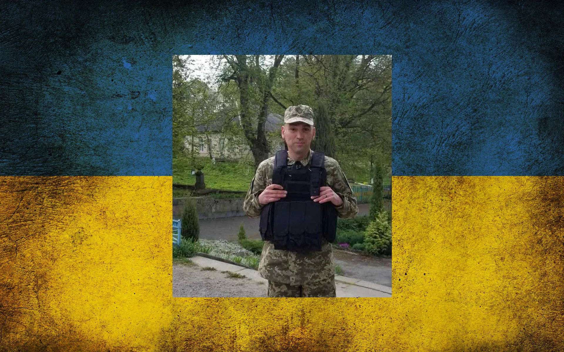 Військовий у бронежилеті на тлі українського прапора