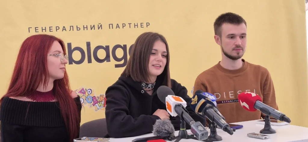 Троє молодих людей на пресконференції перед мікрофонами