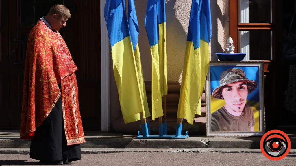 Священник біля портрета загиблого військового та прапорів України
