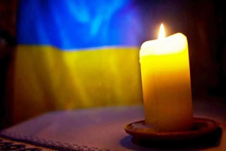 Запалена свічка на тлі прапора України