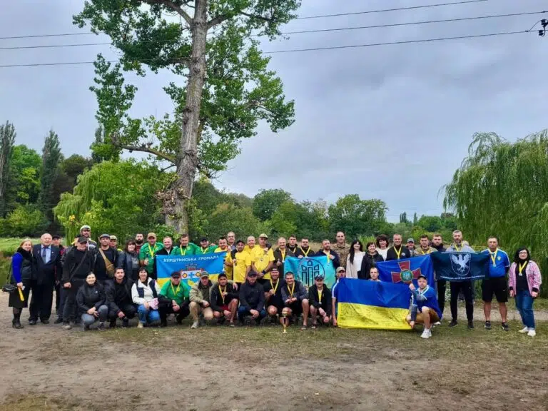 Група людей з українськими прапорами біля великого дерева