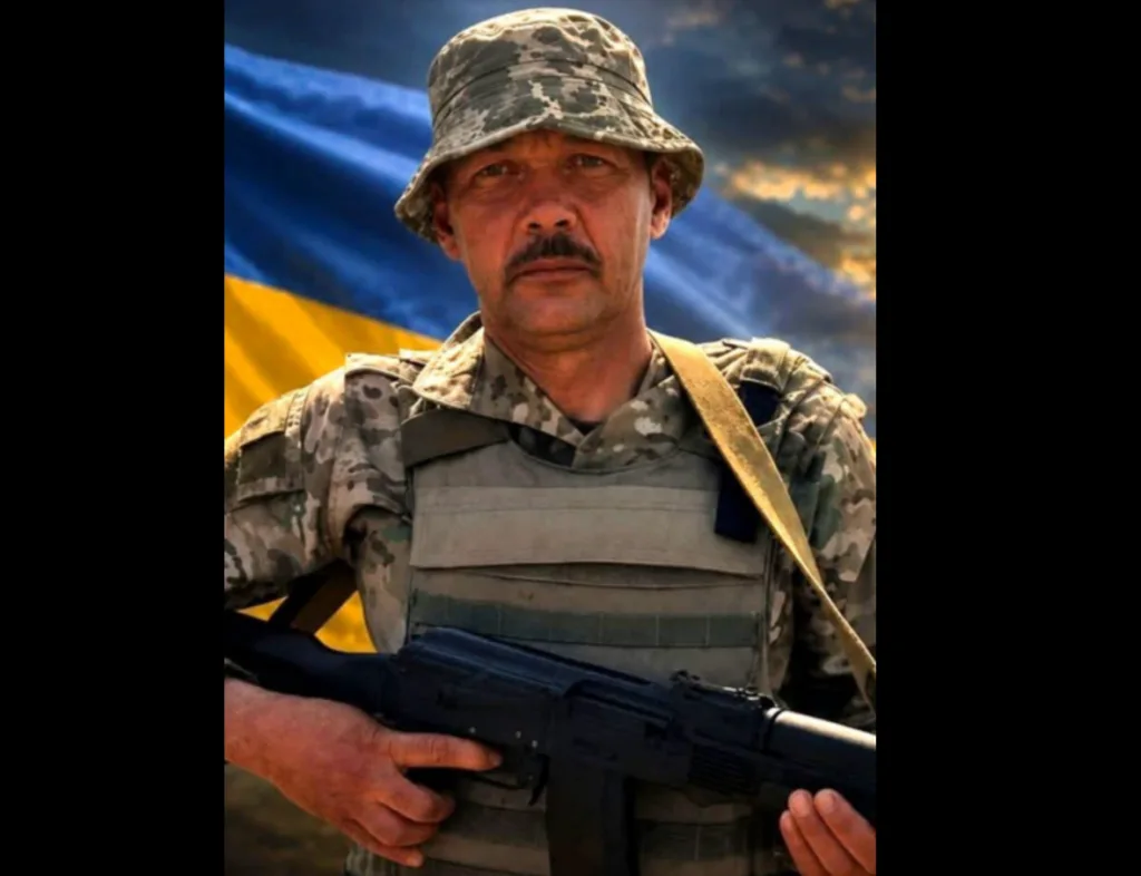 Український військовий з автоматом на тлі прапора