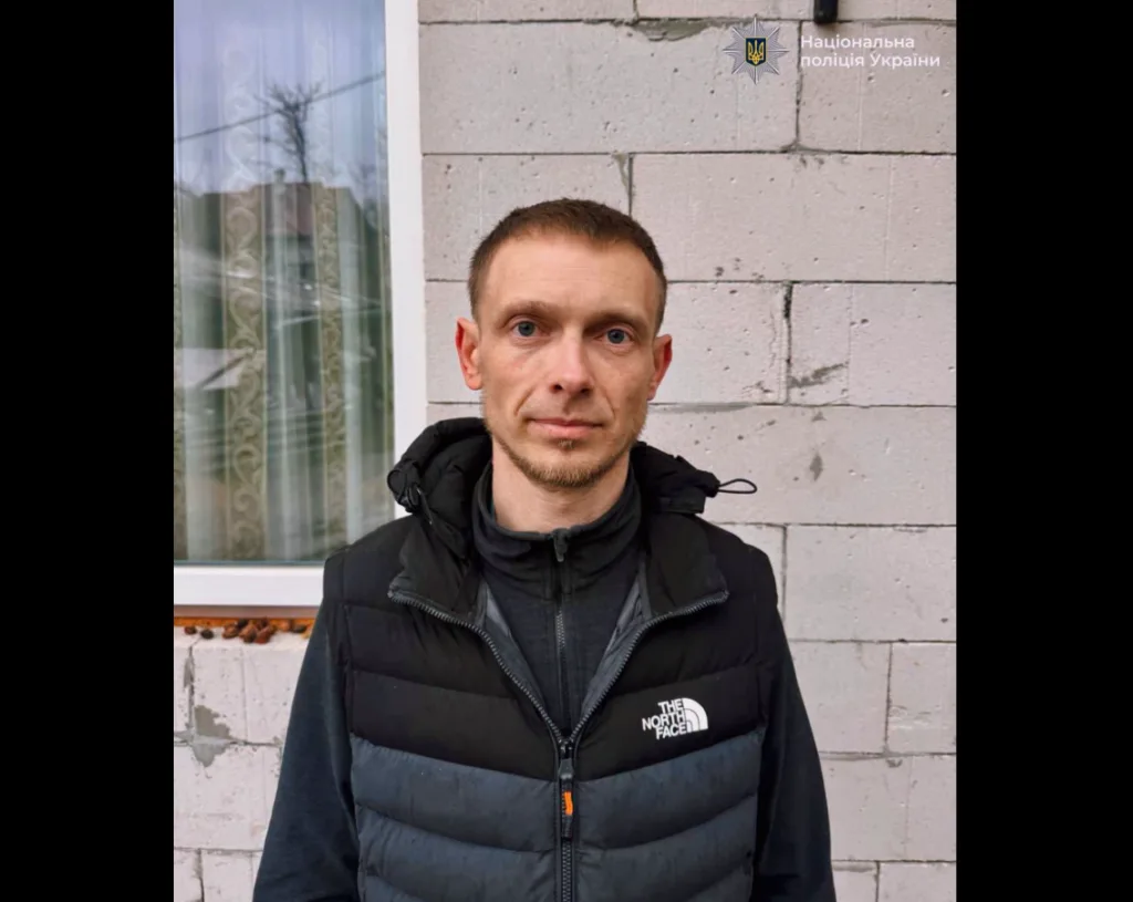 Чоловік у чорному жилеті біля цегляної стіни