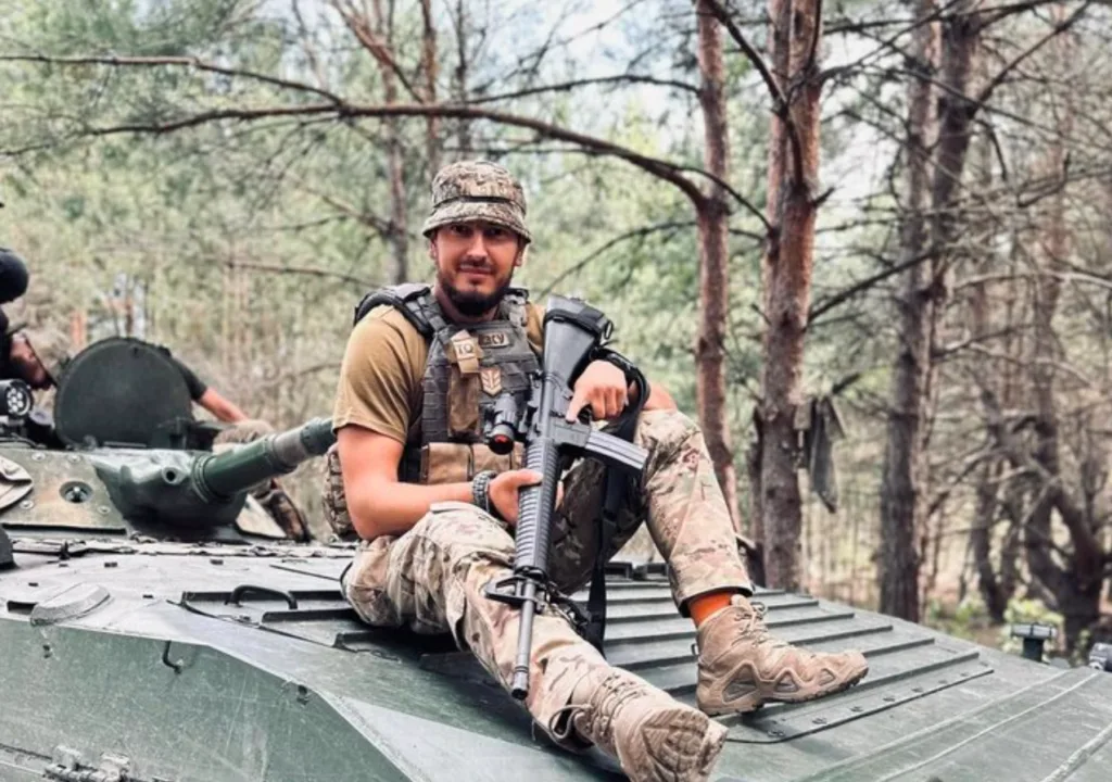 Військовий із гвинтівкою сидить на бронетехніці в лісі