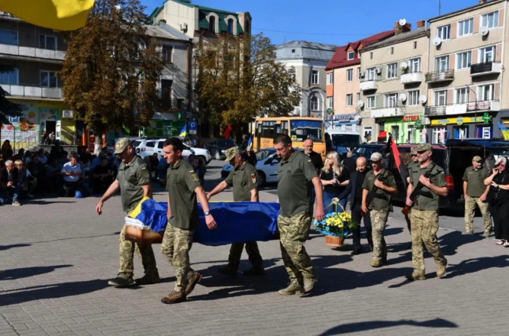 Військові несуть труну, вкриту українським прапором