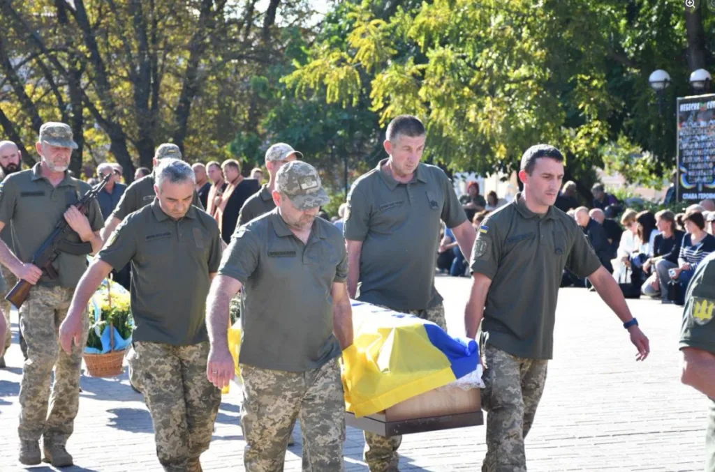 Військові несуть труну, вкриту українським прапором